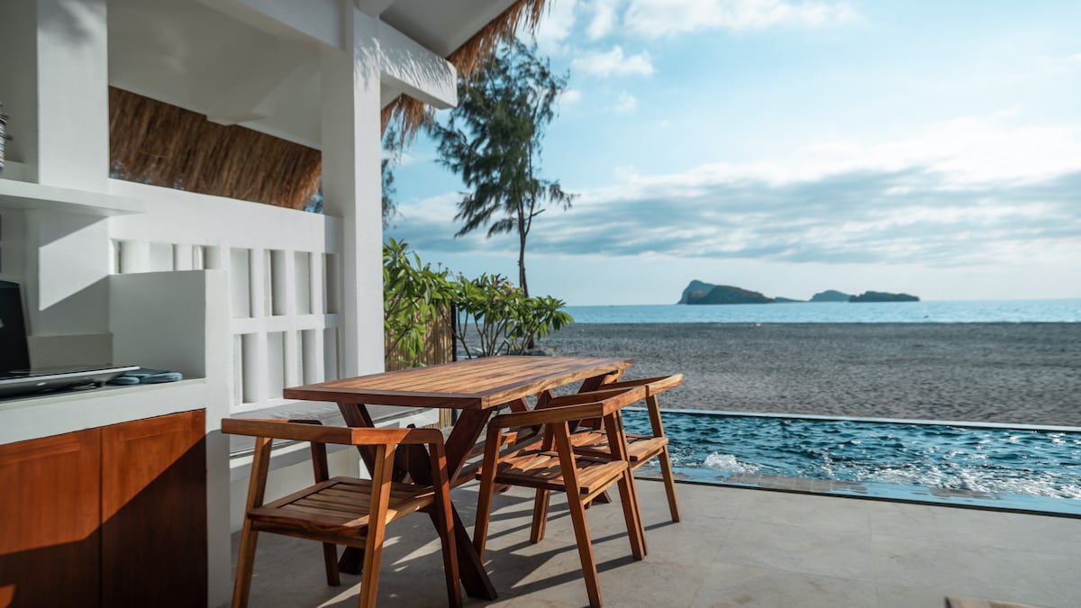 Outdoor teak dining area with pool and ocean view at dusk